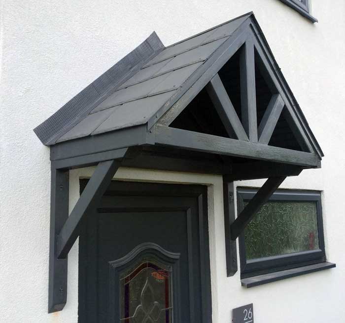 A black-painted all-wood apex-style door canopy installed on a white-painted house